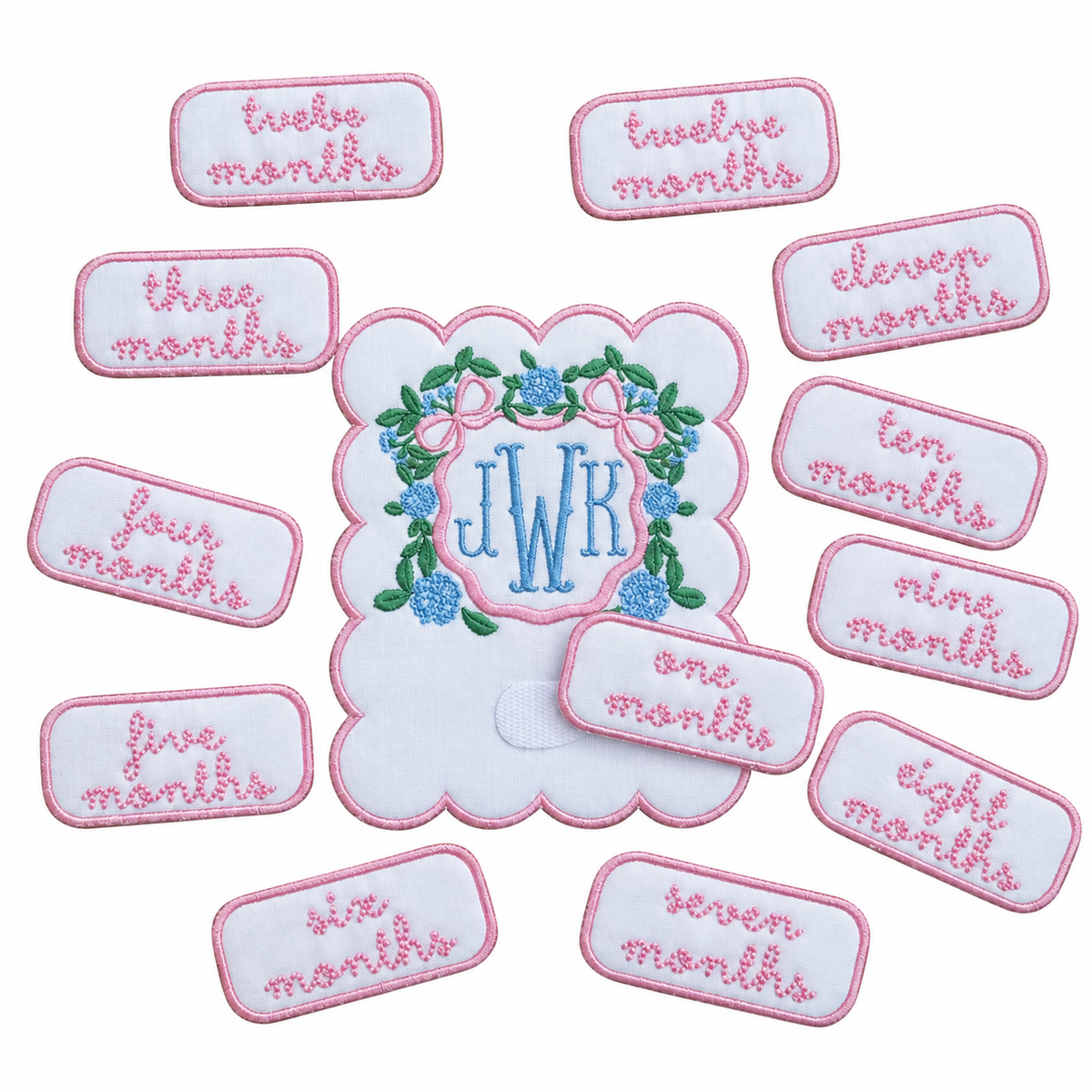 Embroidered monthly milestone card with a blue JWK monogram in a hydrangea wreath with a pink bow, surrounded by pink embroidered month patches