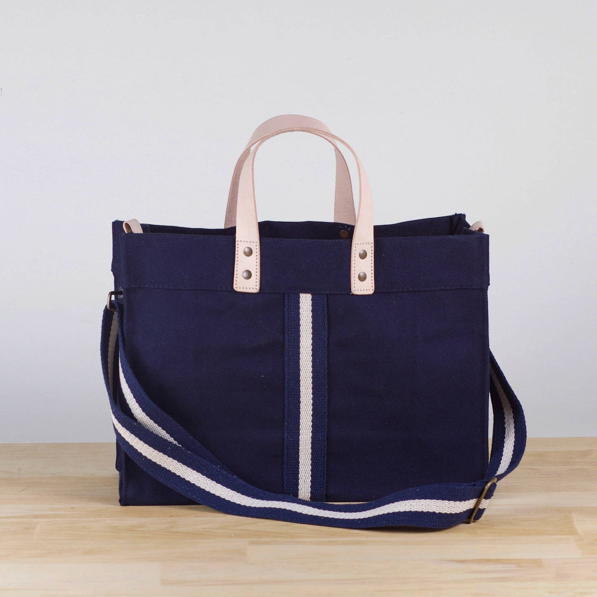 Mini navy canvas box tote with leather handles, a white center stripe, and a navy and white striped detachable strap