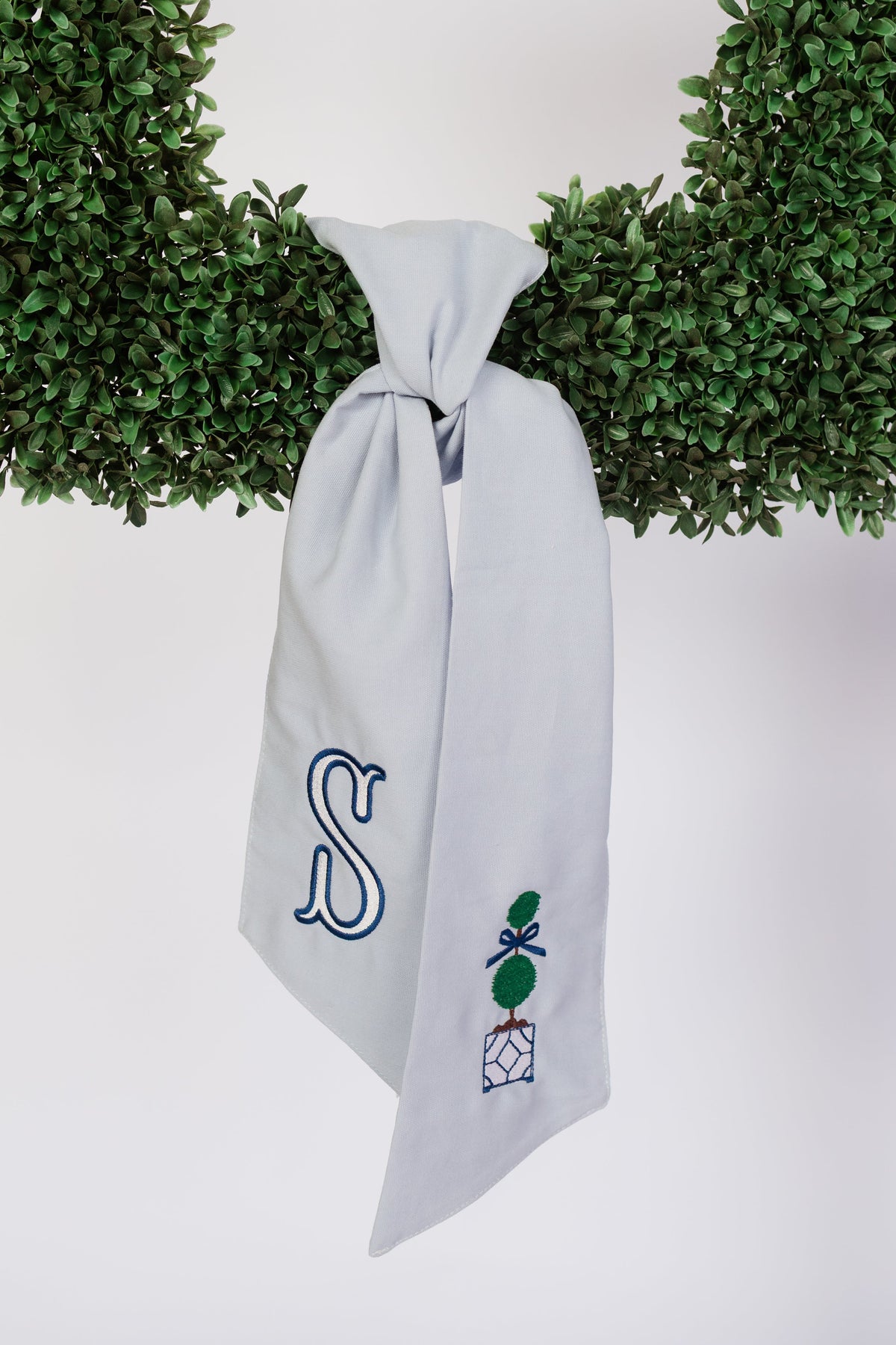 A white sash monogrammed with the letter S, tied on a boxwood wreath