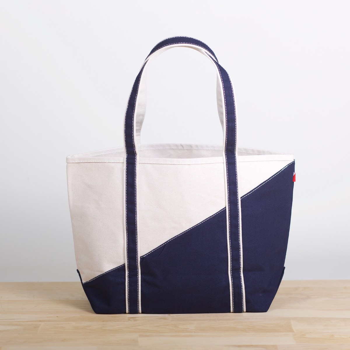 Natural canvas tote with a navy diagonal sail design and navy handles