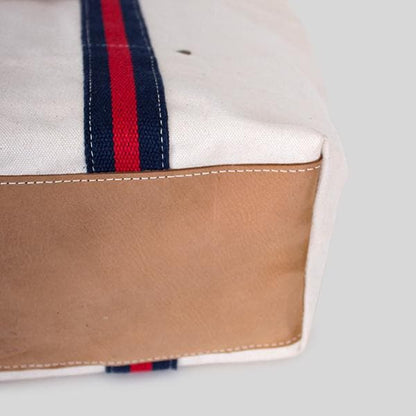 Close-up of the tote's tan leather bottom and navy and red striped strap
