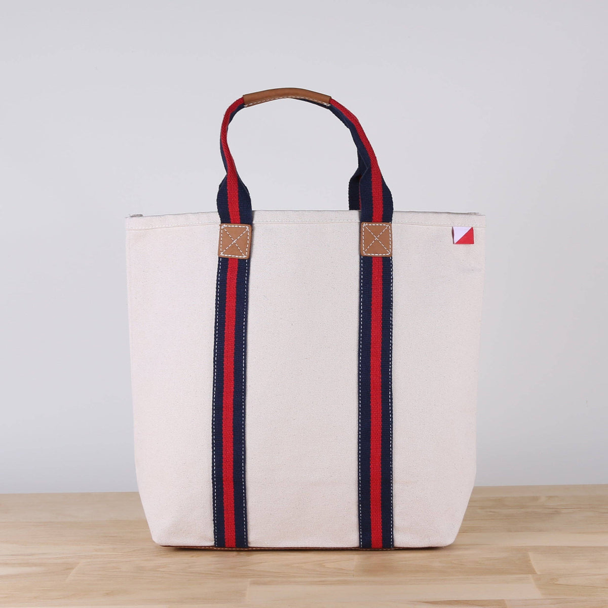 Woman carrying the natural canvas tote with navy and red striped straps at the water's edge